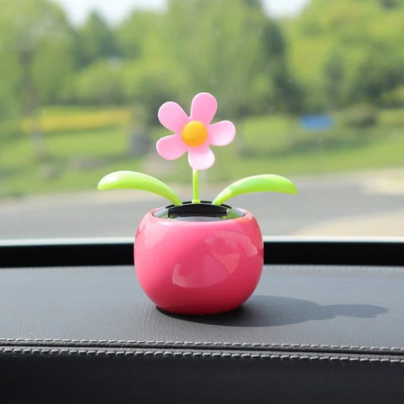 Pink flower-shaped car ornament on a car dashboard with a blurred green outdoor background