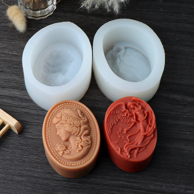 Two white oval silicone soap molds behind tan woman-profile and red winged figure casting examples