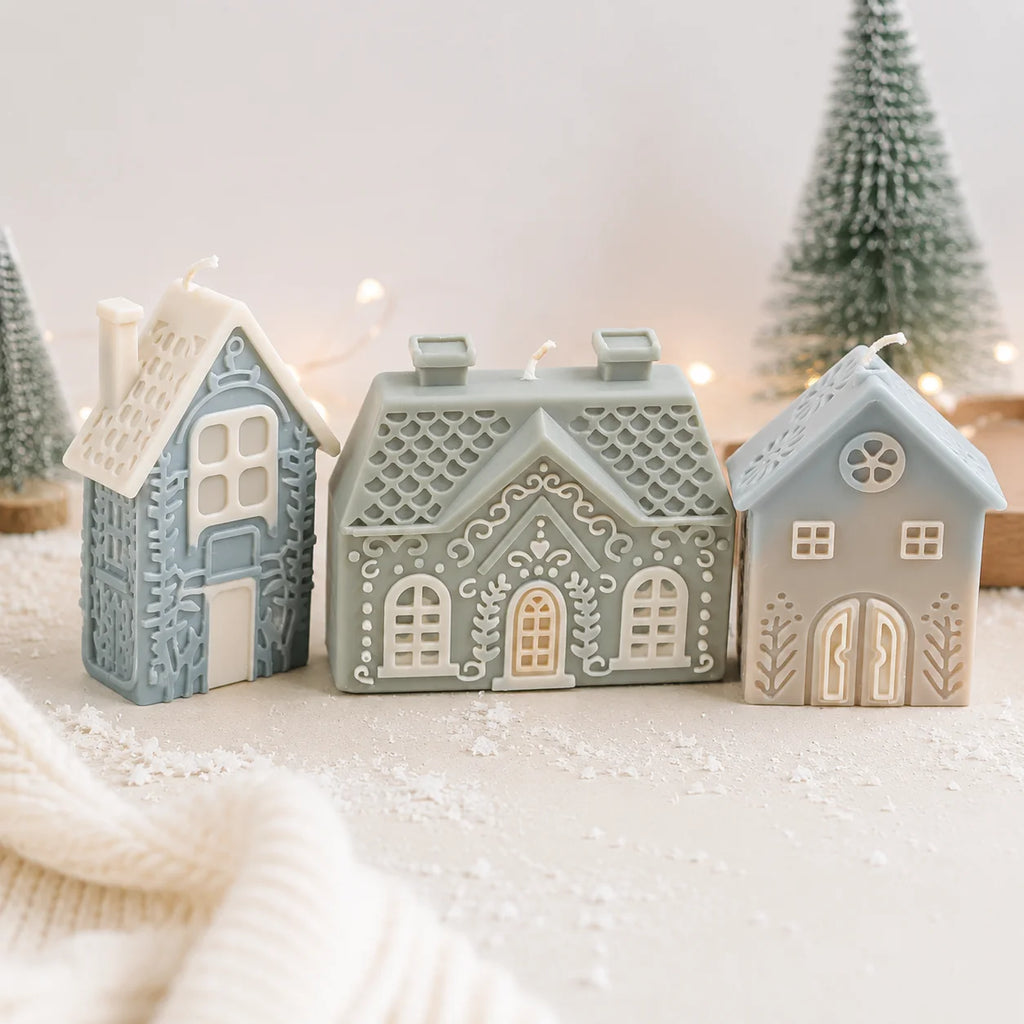 Three blue-gray and green house example candles arranged with miniature snowy trees