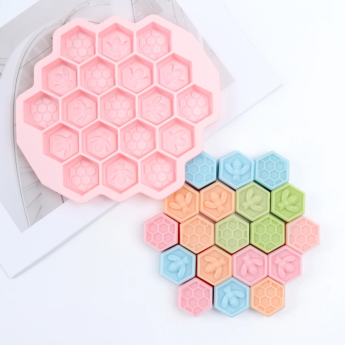 Empty pink hexagonal bee and honeycomb mold beside a cluster of pastel example castings