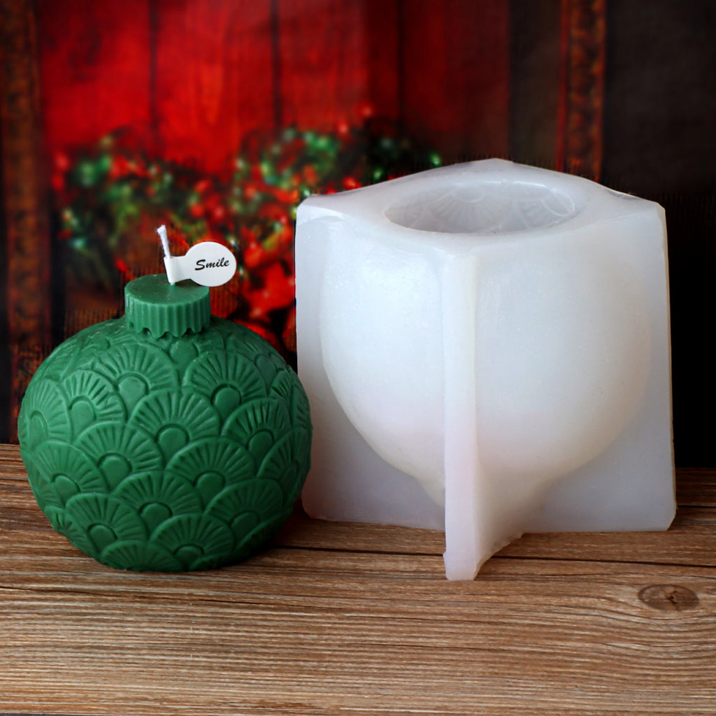 Green fan-pattern ornament-ball example candle beside an opened white silicone mold