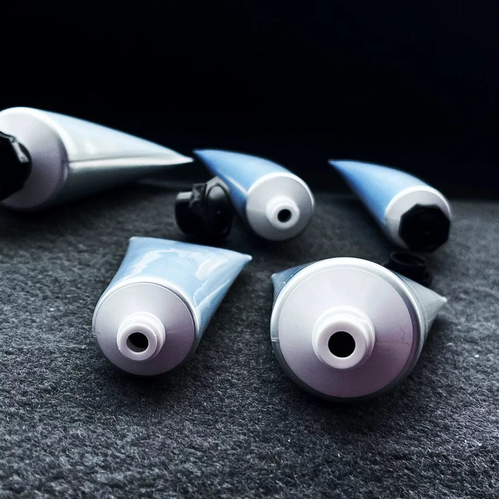 Open silver squeeze tubes showing white threaded openings and black caps