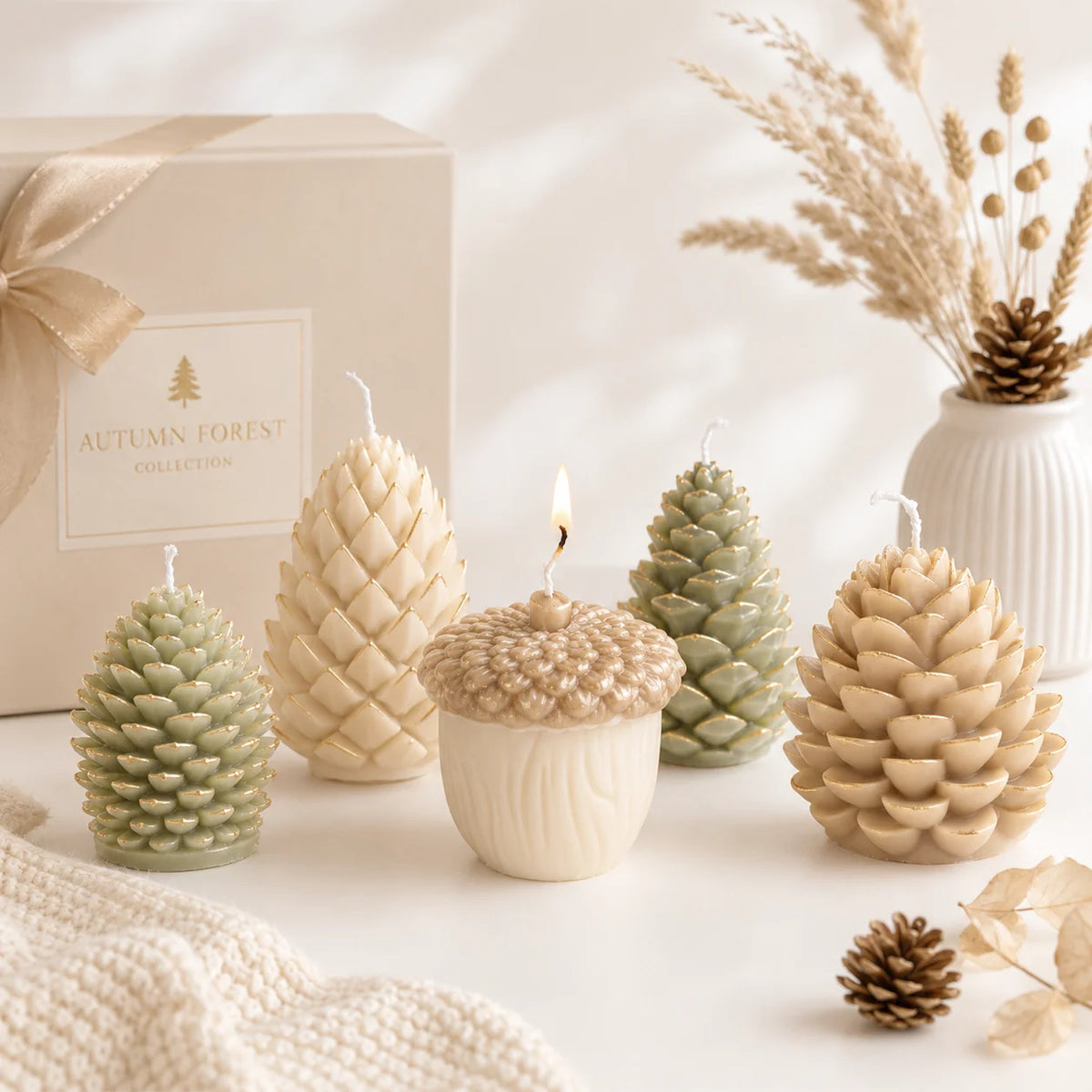 Five pinecone and acorn example candles in ivory, beige and green beside an Autumn Forest display box
