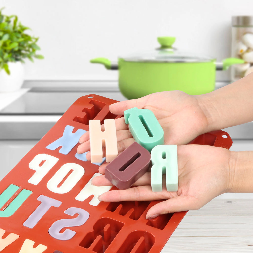 Hands holding four colored letter casting examples above a red alphabet silicone mold