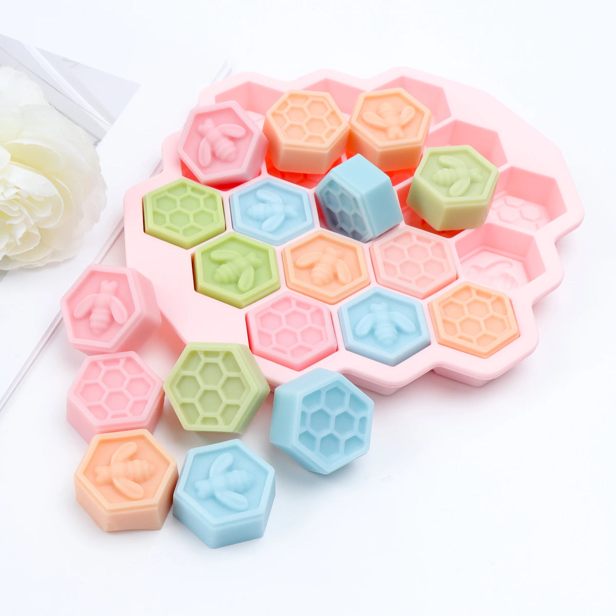 Pink hexagonal bee and honeycomb mold with pastel example castings arranged in and around its cavities