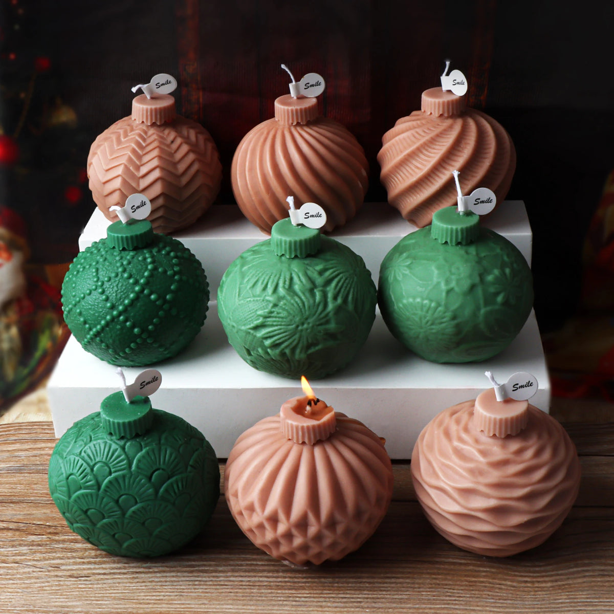 Nine pink and green textured ornament-ball example candles arranged on a stepped white display