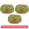 Three variegated yarn skeins in green, gold, purple and white, shown as one package.