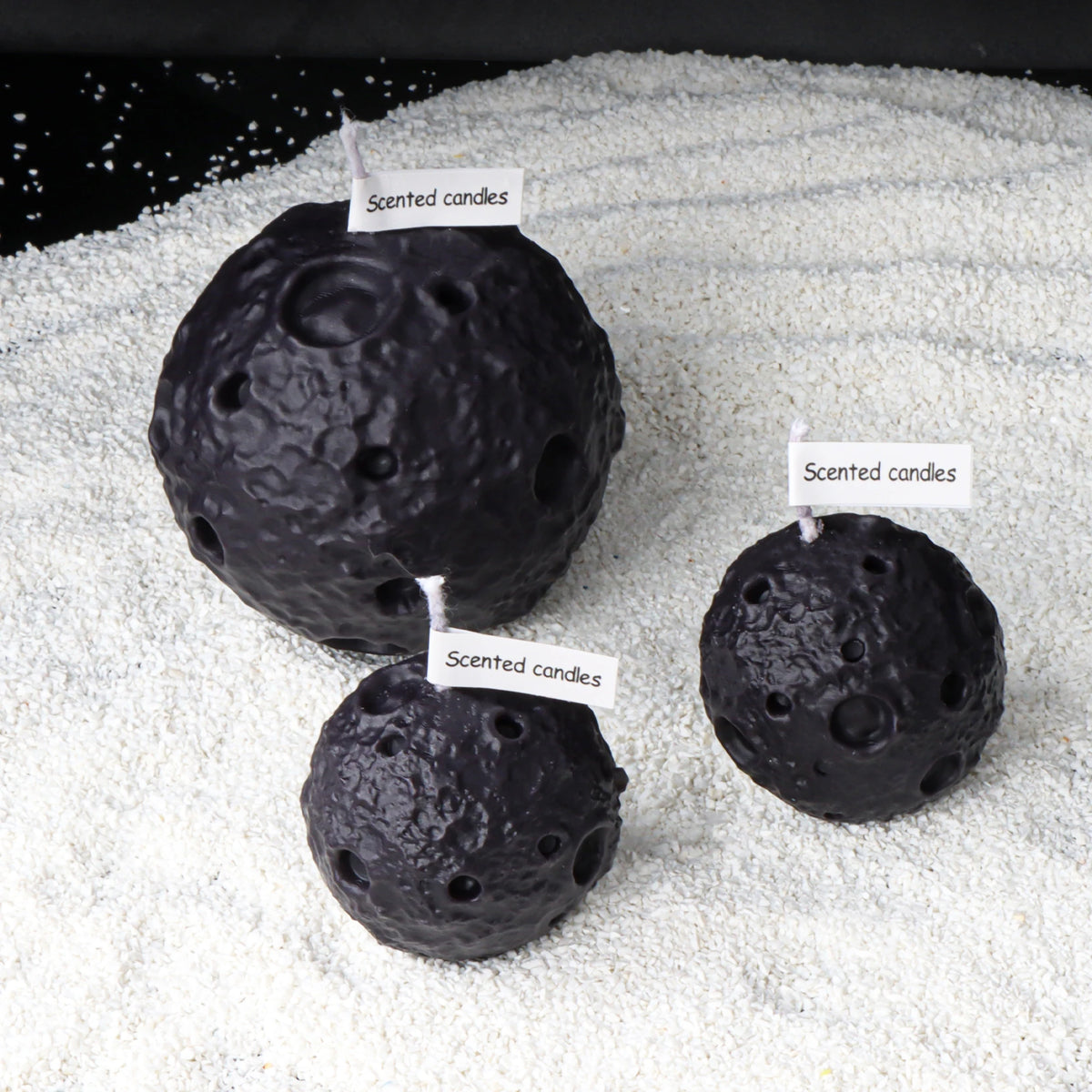 Three black crater-textured moon candles with wicks and paper scent tags