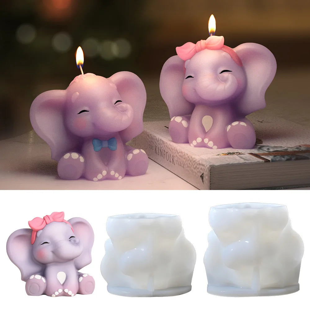 Two lit elephant-shaped candles in pastel purple and pink are shown on a tabletop, with two white silicone mold cavities below. The candles have closed eyes, one with a blue bow tie and one with a pink bow headband, and are presented on a clean white background with a lifestyle tabletop scene above.