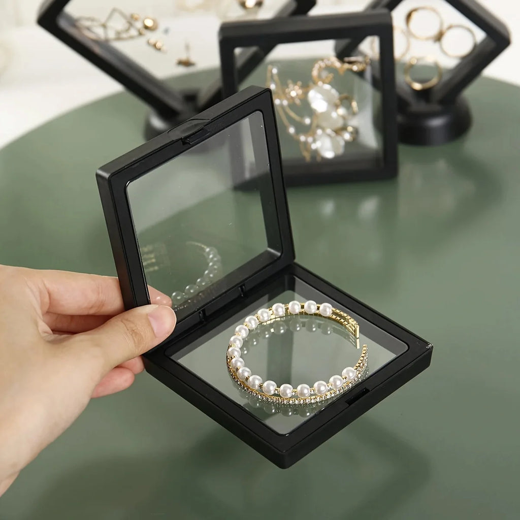Hand holding a black jewelry box with a pearl bracelet inside, on a green surface.