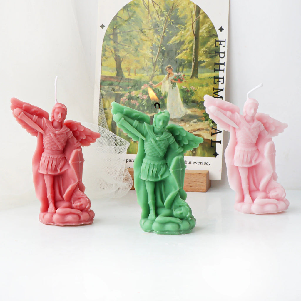 Pink, green and pale pink archangel example candles with spread wings, armor, shield and a figure at the base